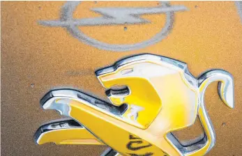  ?? FOTO: DPA ?? Ein Opel-Logo und das Opel-Gelb spiegeln sich in einem Peugeot-Logo: Vor dem Autobauer liegt noch ein schwerer Weg, denn während Opel nach wie vor Verluste schreibt, fährt PSA Gewinne ein.