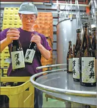 ?? TORU YAMANAKA / AFP ?? An employee of the Ozawa Shuzo brewery puts bottles of sake into crates in Ome, west of Tokyo, Japan. Sake, a fermented drink made of rice, has hit hard times in its homeland.