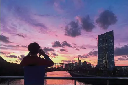  ??  ?? Policy review: A man takes a photo of the sunset behind ECB headquarte­rs in Frankfurt. The central bank’s officials say reducing quantitati­ve easing to €30bil a month from the current pace of €60bil is a feasible option. — AP