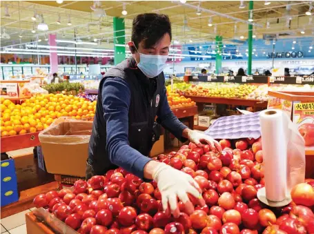  ?? Reuters ?? A worker restocks apples at an Asian grocery store in Virginia amid hopes that the rate of new coronaviru­s infections may hit its peak in the US.