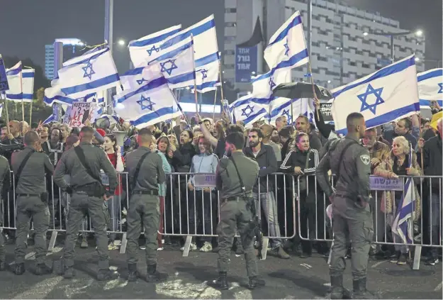  ?? ?? Israeli security forces guard a barrier as left wing activists wave national flags during an anti-government demonstrat­ion in Tel Aviv yesterday