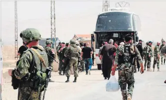  ?? SANA THE ASSOCIATED PRESS ?? This photo released by the Syrian official news agency SANA shows Russian soldiers and Syrian government forces gathering next to a bus during the evacuation of rebel fighters.