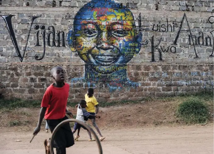  ?? © Tony Karumba/afp ?? Kinderen spelen in een sloppenwij­k in Nairobi. Op de muur achter hen staat een leuze in Swahili die hen ‘oproept om in vrede samen te leven’.