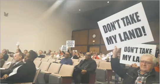  ?? STAFF PHOTO BY MICHAEL SYKES II ?? As County Commission­er Ken Robinson answers a question read off a card submitted at the first quarterly town hall meeting in the commission chambers, Charles County citizens hold up signs in protest of the Watershed Conservati­on District, a...