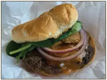  ?? (Arkansas Democrat-Gazette/Eric E. Harrison) ?? Backyard Burgers’ Honey BBQ Burger puts a hefty charcoal-grilled patty, honey barbecue sauce, fried pickles, cheese, red onions and greenery on a brioche-style bun.