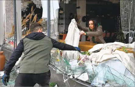  ?? Sergey Bobok AFP/Getty Images ?? PEOPLE carefully remove shards of glass from broken windows of a cafe after a Russian missile attack this week in Kharkiv, Ukraine.