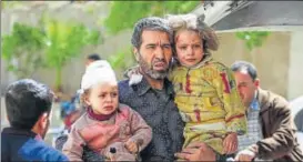  ?? AFP ?? A Syrian man carries injured children after a reported air strike in Hamouria.