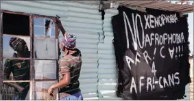  ?? PHOTO: AP ?? A man replaces a broken window at a tavern in Philippi township, on the outskirts of Cape Town, next to a banner that reads: No Xenophobia, No Afrophobia, Africa 4 Africans.