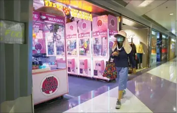  ?? CALVIN NG / CHINA DAILY ?? A woman wearing a hat, a face mask and a face shield to protect herself from the novel coronaviru­s walks past a claw machine arcade in Tseung Kwan O.