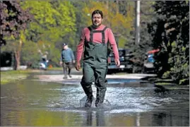  ??  ?? Roberto Acuna walks Wednesday through a flooded street beside his home on Hawthorne Lane in Des Plaines after a large amount of rain fell over the course of a couple days.