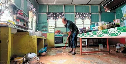  ?? — Bernama ?? Grimy aftermath: Mohd Hasim yusof, 59, cleaning his kitchen, which was covered in mud due to the flood at Kampung sungai Jernih.