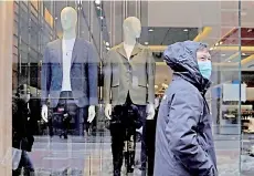  ??  ?? A person wearing a facemask walks past a men’s clothing store on Madison Avenue in New York.