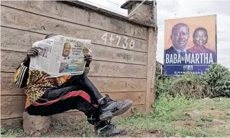  ?? ?? A MAN reads the Daily Nation newspaper while seated near a campaign billboard of Raila Odinga and his running mate Martha Karua, following Kenya’s general election in Nairobi this week. Kenyans are anxiously awaiting the results of the elections. | AFP