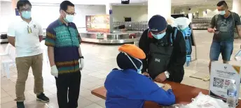  ??  ?? Lee (second left) watches a passenger having his details taken upon arrival at Miri Airport.