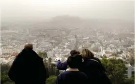  ??  ?? ATHENS: Tourists take a look of central Athens with the Acropolis hill (top) engulfed in African dust carried by strong southerly winds as they stand on Lycabettus hill yesterday. A day after Greece appeared on a collision course with its creditors,...