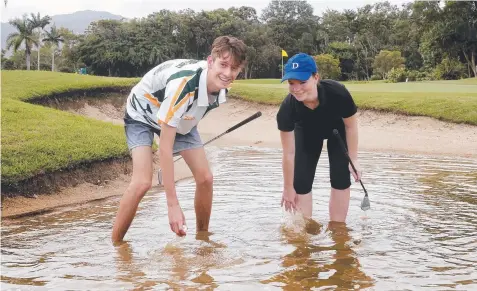  ?? Picture: ANNA ROGERS ?? SUNK: Griffin Haseldine and Emma Anderson search for a golf ball in the flooded bunker at Cairns Golf Club.