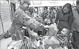  ?? MARK THIESSEN/AP ?? Alaska National Guard Staff Sgt. Joseph Sallaffie hands a gift bag to Corban Jimmy while Marlene Black looks on during Santa’s visit to Napakiak, Alaska.