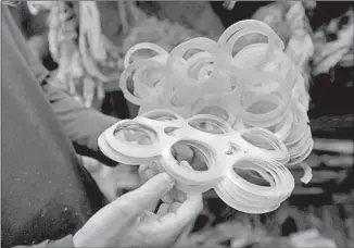  ??  ?? PETERS thumbs through the plastic 6-pack holders that are part of the collection of litter he keeps at his Venice home. He tries to pick up plastic first, he said, since it can harm marine life.