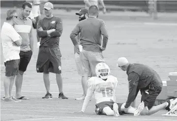  ?? TAIMY ALVAREZ/SUN SENTINEL ?? A trainer works on new practice squad receiver Travis Rudolph during practice Wednesday. In the background is Dolphins head coach Adam Gase talking with Cubs first baseman Anthony Rizzo, a Stoneman Douglas alum.