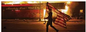 ?? JULIO CORTEZ / AP ?? A protester carries a U.S. flag upside down, a sign of distress, next to a burning building Thursday, in Minneapoli­s.