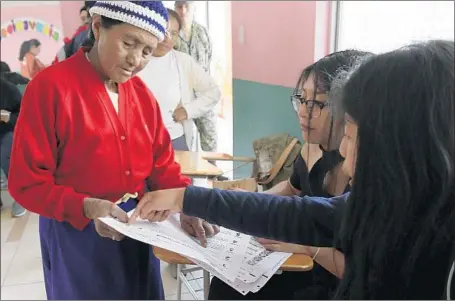  ?? Dolores Ochoa Associated Press ?? A VOTER gets her question answered in Quito, Ecuador’s capital. Sixty-four percent of voters opted to end unlimited presidenti­al runs.