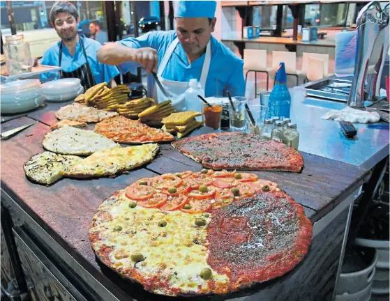  ??  ?? Para todos los gustos. La enorme pizza de Angelín es de mozzarella, cancha y napolitana. Para acompañarl­a, una porción de fainá.