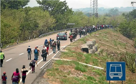  ??  ?? Central American migrants travelling in a caravan to the US border walk as police ride alongside them through Tonala, Chiapas state, Mexico.