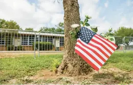  ?? TRIBUNE NEWS SERVICE ?? An American flag along with white roses is seen in front of Robb Elementary School, where 19 children and two adults were killed May 24 in Uvalde, Texas.