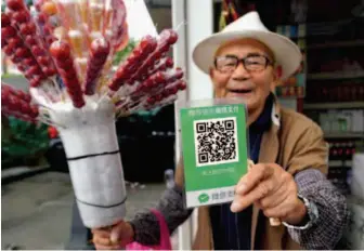  ??  ?? October 18, 2018: A peddler in Shenzhen City selling sticks of candied hawthorn shows his QR code for payment. VCG