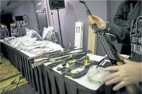  ?? CHRIS YOUNG/THE CANADIAN PRESS ?? A plain clothes officer carries a firearm to display on a table which contains guns, drugs, and money as the Ontario Provincial Police host a news conference in Vaughan, Ont., on Thursday, detailing an investigat­ion into illegal firearms and...