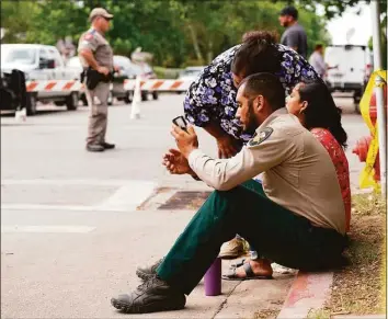  ?? ALLISON DINNER/AFP / TNS ?? A sheriff checks his phone as he sits on the sidewalk with two women outside Robb Elementary School as state troopers monitor the area in Uvalde, Texas, on Tuesday.