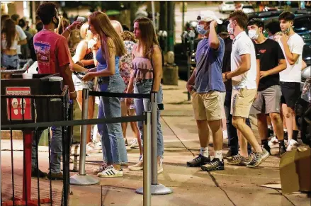  ?? JOSHUA L. JONES / ATHENS BANNER-HERALD VIA AP ?? A doorman checks customers’ temperatur­es as they wait to enter Sandbar in downtown Athens last month. On Tuesday, the state Department of Public Health reported 2,101 net new cases of the coronaviru­s, and 106 net new deaths. More than 258,000 Georgians have contracted the coronaviru­s and 5,262 have died from the disease, according to the latest state public health data.