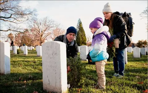  ?? Maansi Srivastava / For The Washington Post ?? Army Maj. Jerry Champion talks to his daughter Charlotte, 4, about what it means to serve in the Army, as his wife, Alyssa Champion, listens. They were part of the annual Wreaths Across America at Arlington National Cemetery, a national holiday wreath-laying ceremony held at more than 1,600 military cemeteries across the United States and in 26 countries.