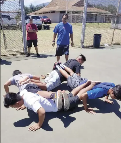  ?? Photo courtesy of Lawrence Pagaduan ?? Maui High School air riflery coach Lawrence Pagaduan looks on as members of his team participat­e in a team-building exercise in which they must all do push-ups at the same time.