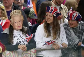  ?? Yui Mok, PA via The Associated Press ?? A girl wearing a cutout face mask of Queen Elizabeth II is among people gathered for the pageant in front of Buckingham Palace.