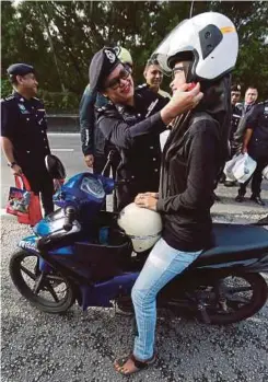  ??  ?? SHAFA’ATON memakaikan topi keledar kepada pengguna motosikal pada majlis pelancaran Op Selamat 14.