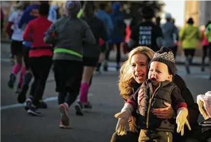  ?? Marie D. De Jesús photos / Houston Chronicle ?? Jessica McCauley and her 22-month-old son. Wagner. wait in the cold Sunday during the Chevron Houston Marathon. While runners sported participan­t numbers, spectators packed on the layers to keep warm.