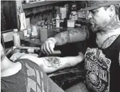  ?? WILSON RING/AP ?? Alexander Lawrence, right, prepares to cover up a tattoo that contained a swastika on the arm of Dylan Graves.