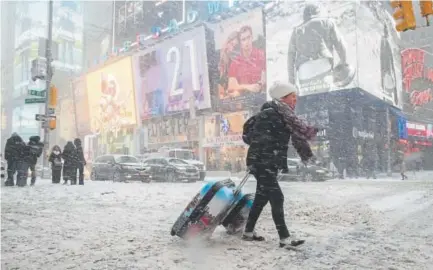  ?? Mary Altaffer, The Associated Press ?? Rebecca Hollis of New Zealand drags her suitcases through Times Square in a snowstorm on her way to a hotel Thursday in New York.