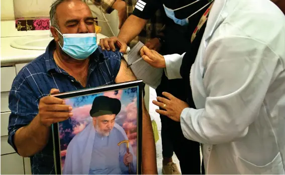  ?? Photo: Hadi Mizban/AP ?? A follower of populist Shiite cleric Muqtada al-Sadr holds a picture of him while receiving a dose of the Chinese Sinopharm coronaviru­s vaccine at a clinic in Sadr City, Baghdad. Iraq’s vaccine rollout had been faltering for weeks.