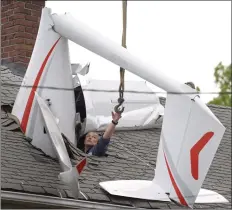  ?? H John Voorhees III / Hearst Connecticu­t Media ?? Chris Cunningham, of Colonial Air in New Bedford, Mass., reaches for a hook being lowered by a crane brought in to remove a 2016 Alisport Silent 2 Electro glider from the roof of a house on Golden Hill Avenue. The glider crashed through the roof on Tuesday.