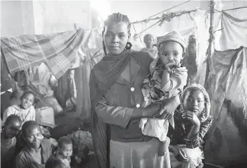  ??  ?? Samira,a displaced Ethiopian, holds one of her seven children in front of the tiny space she shares with other families at the Gedeb site. — Photo by Olivia Headon