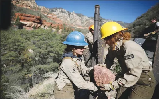  ?? (AP/Arizona Daily Sun/Jake Bacon) ?? Crew leader Hannah Green (left) takes a boulder from crew member Kendel Godfrey on Oct. 20 as the two work to block holes in a fence along Highway 89A in Oak Creek Canyon near Sedona, Ariz.