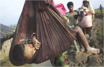  ??  ?? A Rohingya child is carried on a sling while his family walks through rice fields after crossing the border into Bangladesh near Cox’s Bazar’s Teknaf area yesterday. — AP