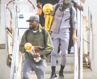  ?? Jessica Christian / The Chronicle ?? Kevin Durant carries his NBA Finals MVP trophy and Stephen Curry the NBA championsh­ip trophy as the Warriors arrive in Oakland, fresh off winning the team’s third title in four years.