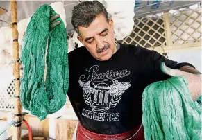  ??  ?? Manual labour: Rihawi dipping silk threads into green dye at his workshop in Damascus. — AFP