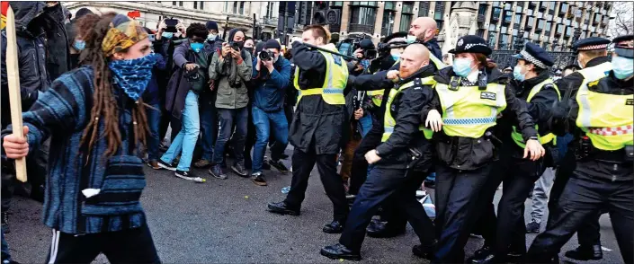  ??  ?? STAND-OFF: A masked protester carrying a sharpened piece of wood walks menacingly towards police as a rally in Parliament Square turns to violence yesterday. At least one officer was injured