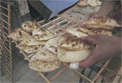  ?? NARIMAN EL-MOFTY/AP ?? A worker collects Egyptian traditiona­l “baladi” flatbread at a bakery in Cairo, Egypt — one of many places in Africa, Asia and Europe that rely on food grown in the fertile Black Sea region threatened by Russia’s invasion of Ukraine.