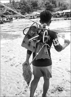  ??  ?? Thiha Tway, a Moken fisherman, heading home while carrying his fishing gear and a pufferfish he caught in Nyaung Wee village. — AFP photos