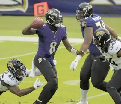  ?? KARL MERTON FERRON/BALTIMORE SUN PHOTOS ?? Surrounded by Jaguars outside linebacker K’Lavon Chaisson, left, and defensive end Dawuane Smoot, right, Ravens quarterbac­k Lamar Jackson looks for an open receiver during a Dec. 20, 2020, game at M&T Bank Stadium.